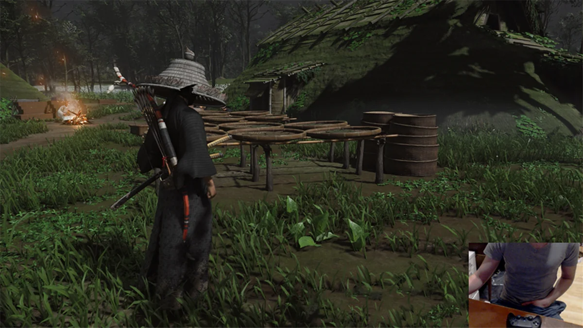 Ghost of Tsushima: Jin mit Strohhut in einem nächtlichen Dorf, unten rechts die Kamera vom Stream